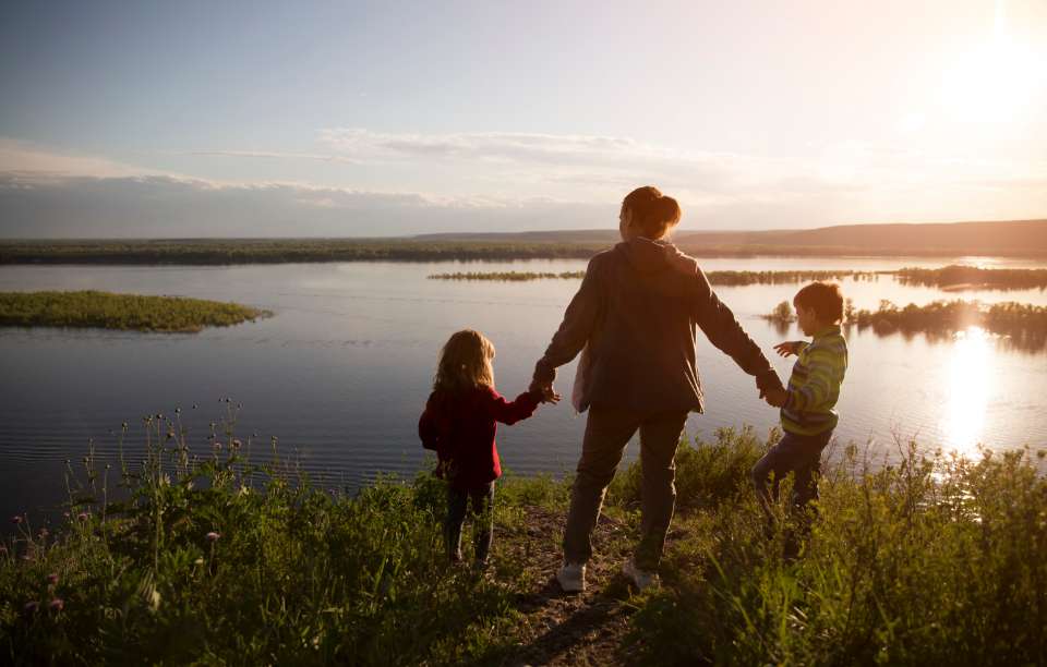 a person and 2 children holding hands whilst watching the sun set over a wetlands area