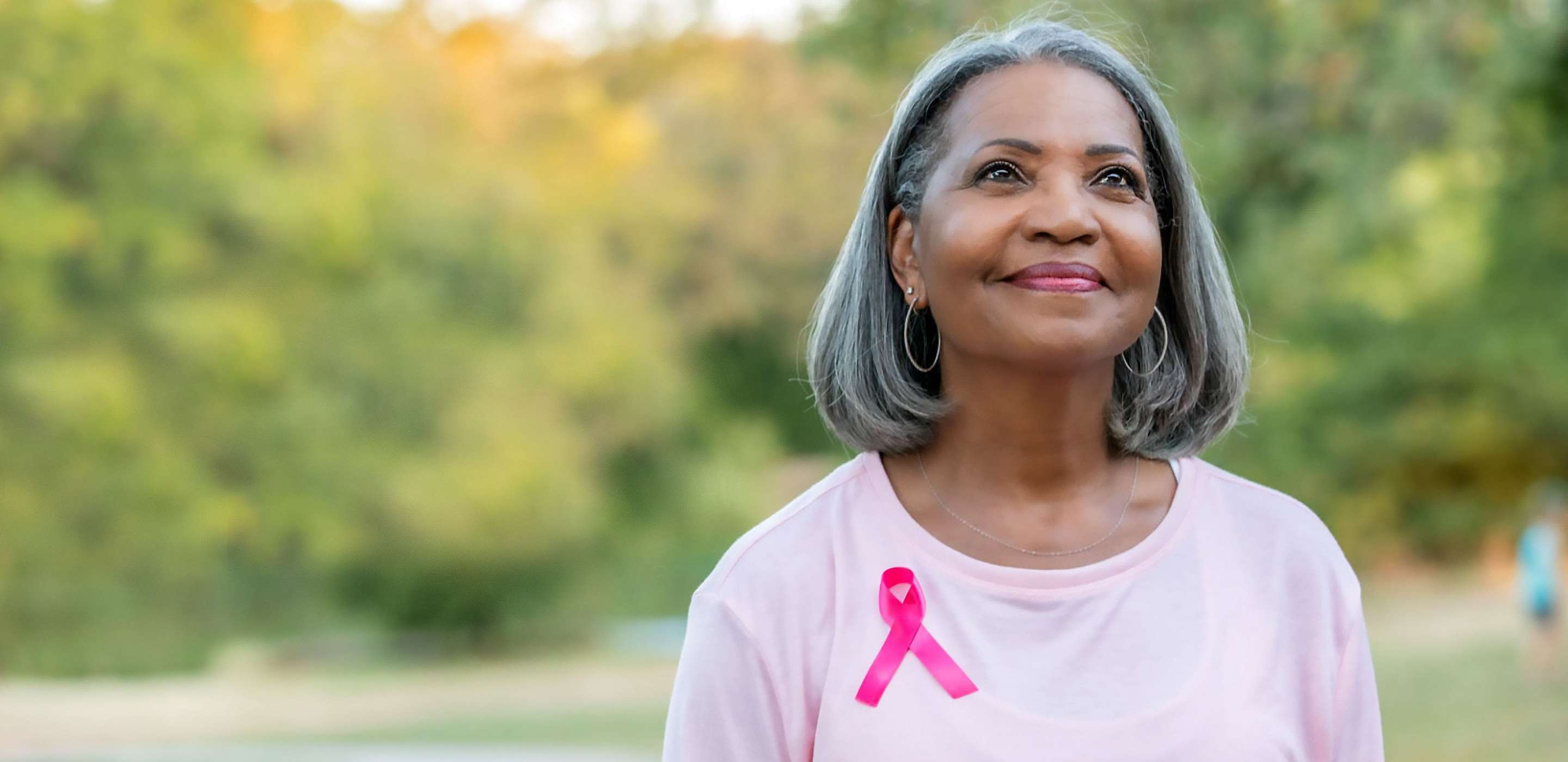 a person smiling. they are wearing a breast cancer research ribbon.